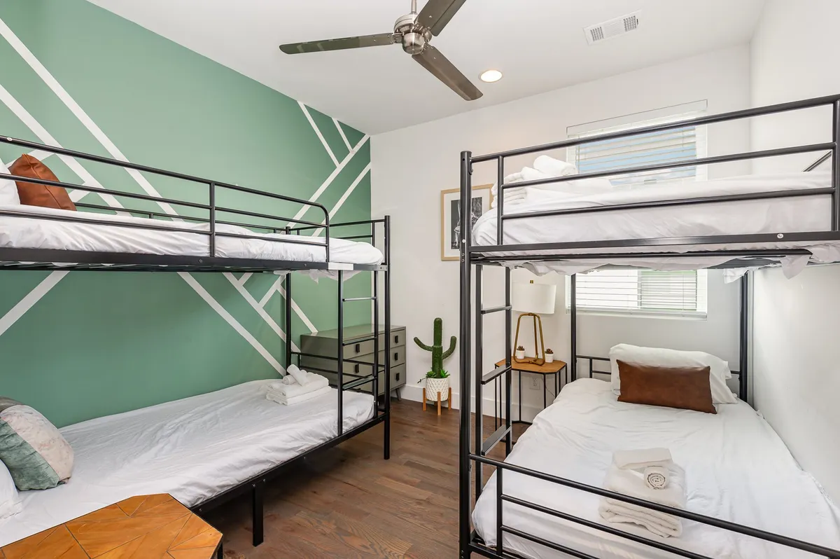 A cheerful bedroom featuring cozy bunk beds set against a green accent wall, with modern lighting and playful cactus decor. The space is designed for group fun, with enough room for reading, playing games, and late-night storytelling sessions.