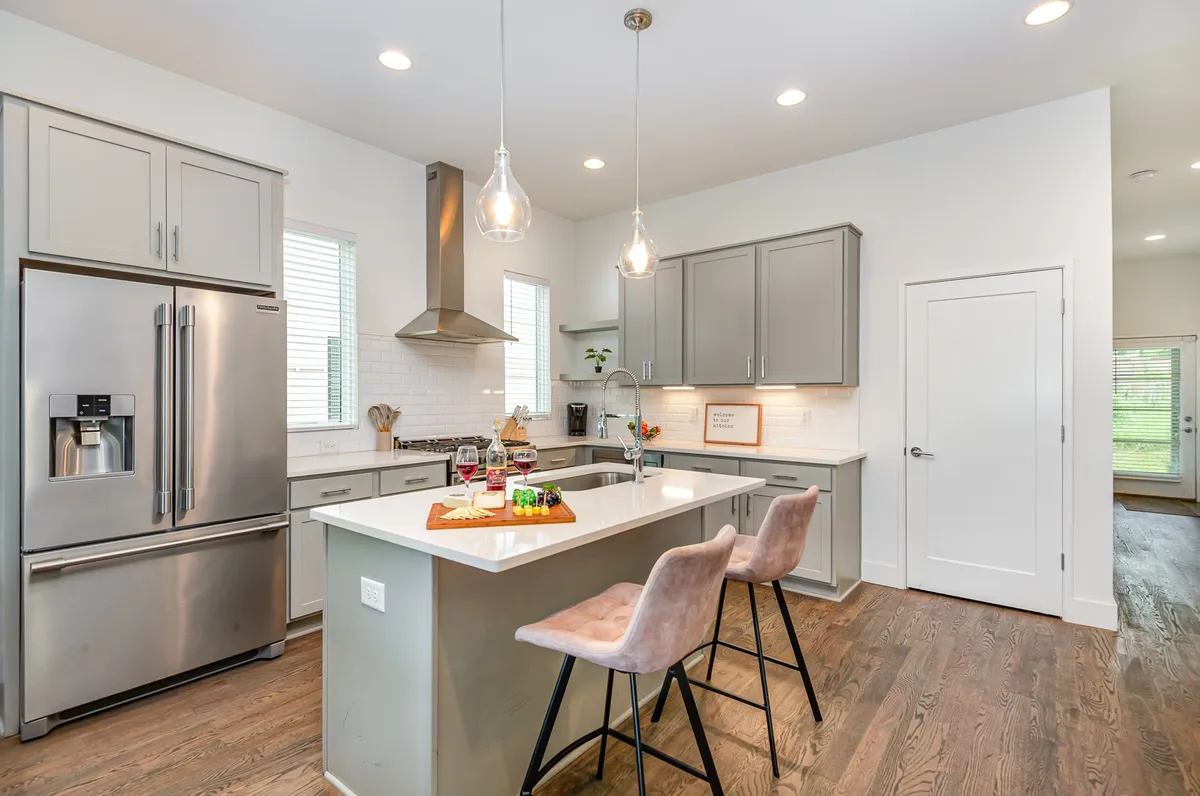 A bright, cheerful kitchen with a large island countertop, bar stools, and modern appliances, illuminated by window light. The setup is ideal for family gatherings, cooking together, or sharing meals after a day of local exploring.