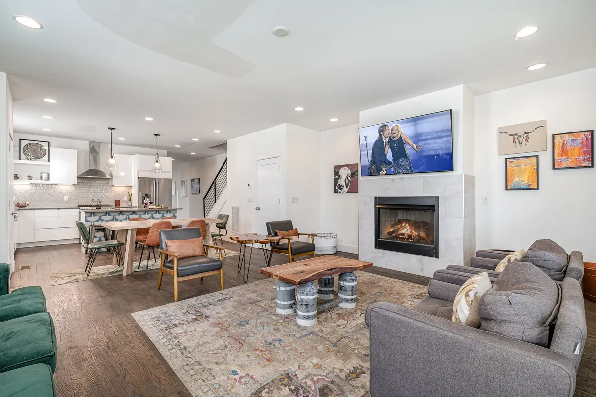 A cozy living room featuring a fireplace, comfortable seating, coffee table, wall art, and a TV. The room is arranged for socializing or relaxing, ideal for gatherings and group activities. The inviting decor and spaciousness reflect a welcoming atmosphere.