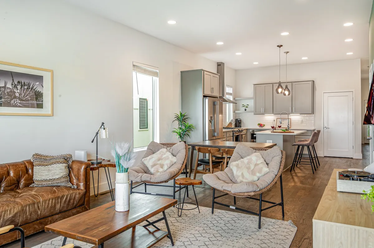 A stylish living space featuring a leather sofa, hanging light fixtures, a dining table, and a kitchen island. The layout encourages social interaction and casual meetings, blending comfort with a contemporary atmosphere.