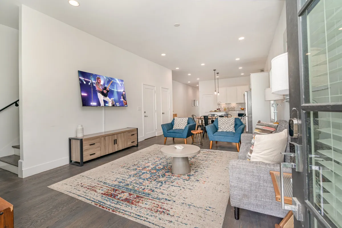 A comfortable living room with a television displaying a live performance, blue accent chairs, and a central coffee table. The setup is perfect for after-hours relaxation, entertainment, or team-building activities like watching a concert together.