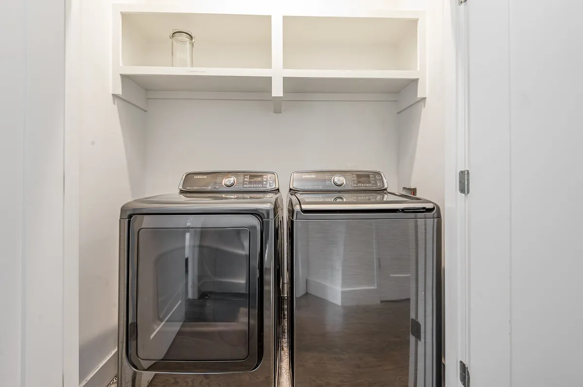 A practical laundry area equipped with washer and dryer units and neatly organized shelves above, making chores easy and accessible for families during their stay.