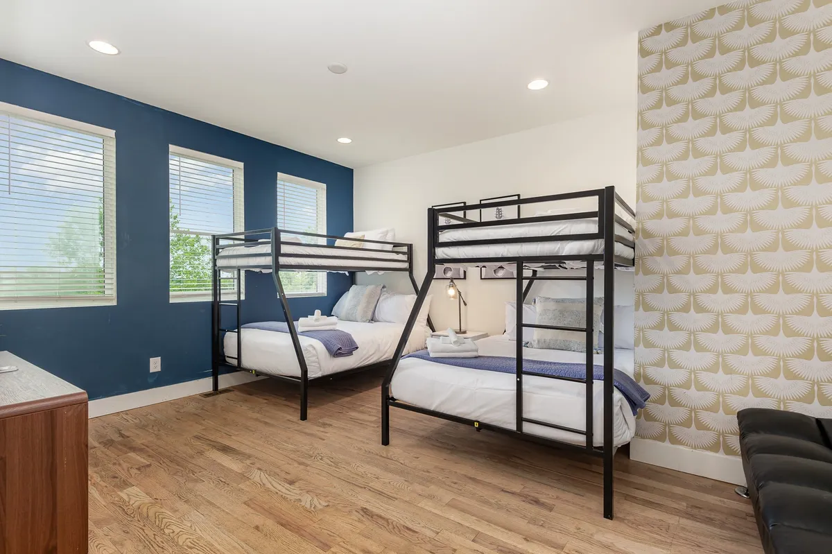 A vibrant bedroom with multiple bunk beds, textured wallpaper, and large windows. The environment is playful and relaxed, ideal for groups to bond, read, or socialize together.