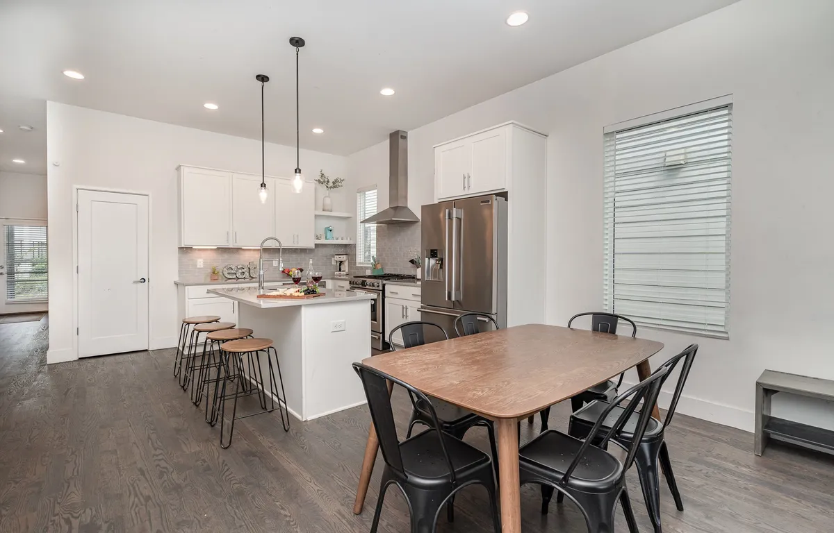 A bright, vibrant kitchen and dining area showcasing a kitchen island, dining table, striking light fixtures, and stainless steel appliances. The space is set up for family meals, group cooking, and entertaining guests.