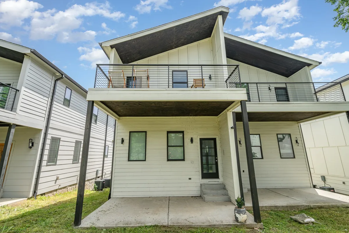 An inviting balcony with comfortable chairs and clean, modern architectural lines, overlooking a landscaped yard. The space is designed for outdoor gatherings, offering a seamless transition from indoor social areas to the open air.
