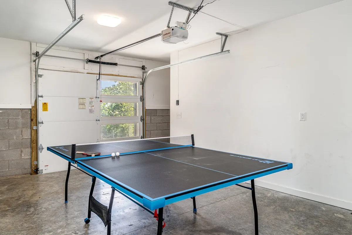 A dedicated game room featuring a ping pong table, garage doors, and a concrete floor, creating a casual and energetic environment perfect for group fun and friendly competition.