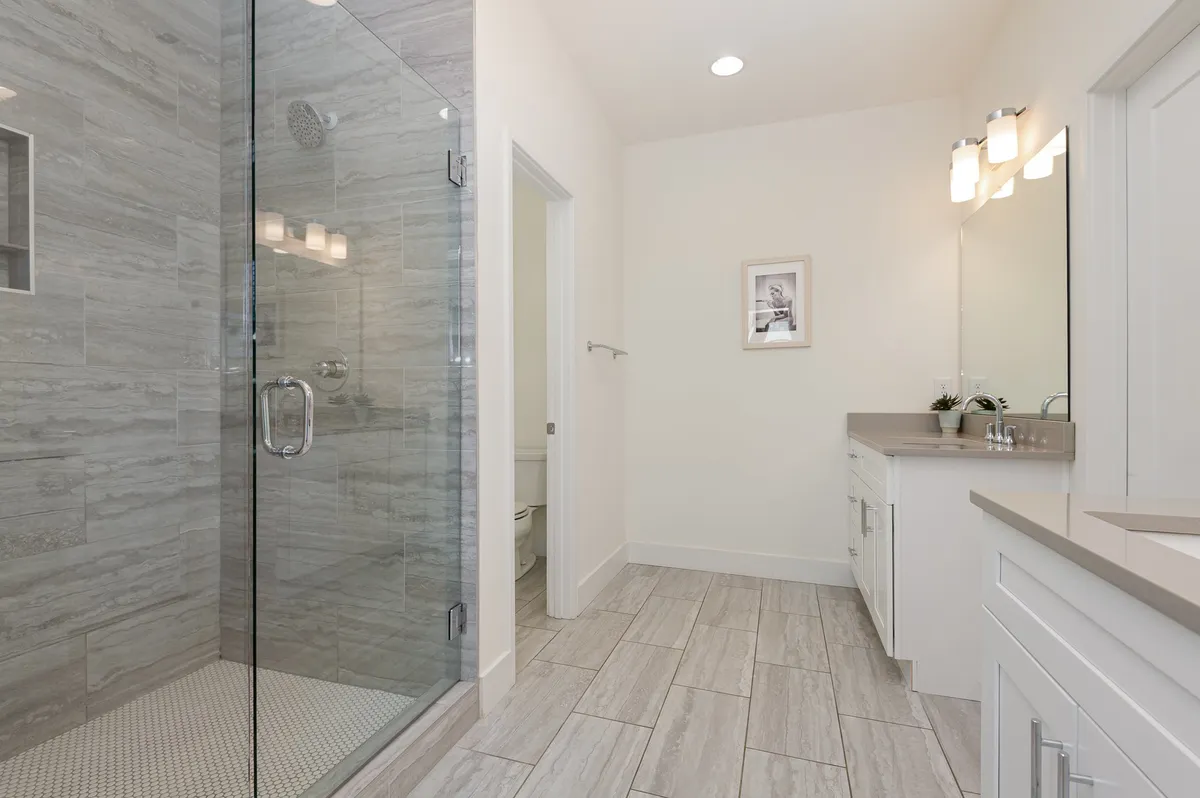 A modern bathroom featuring a glass shower enclosure, double vanity, and framed artwork. The mood is serene, offering ample space for personal grooming and relaxation after a long day.