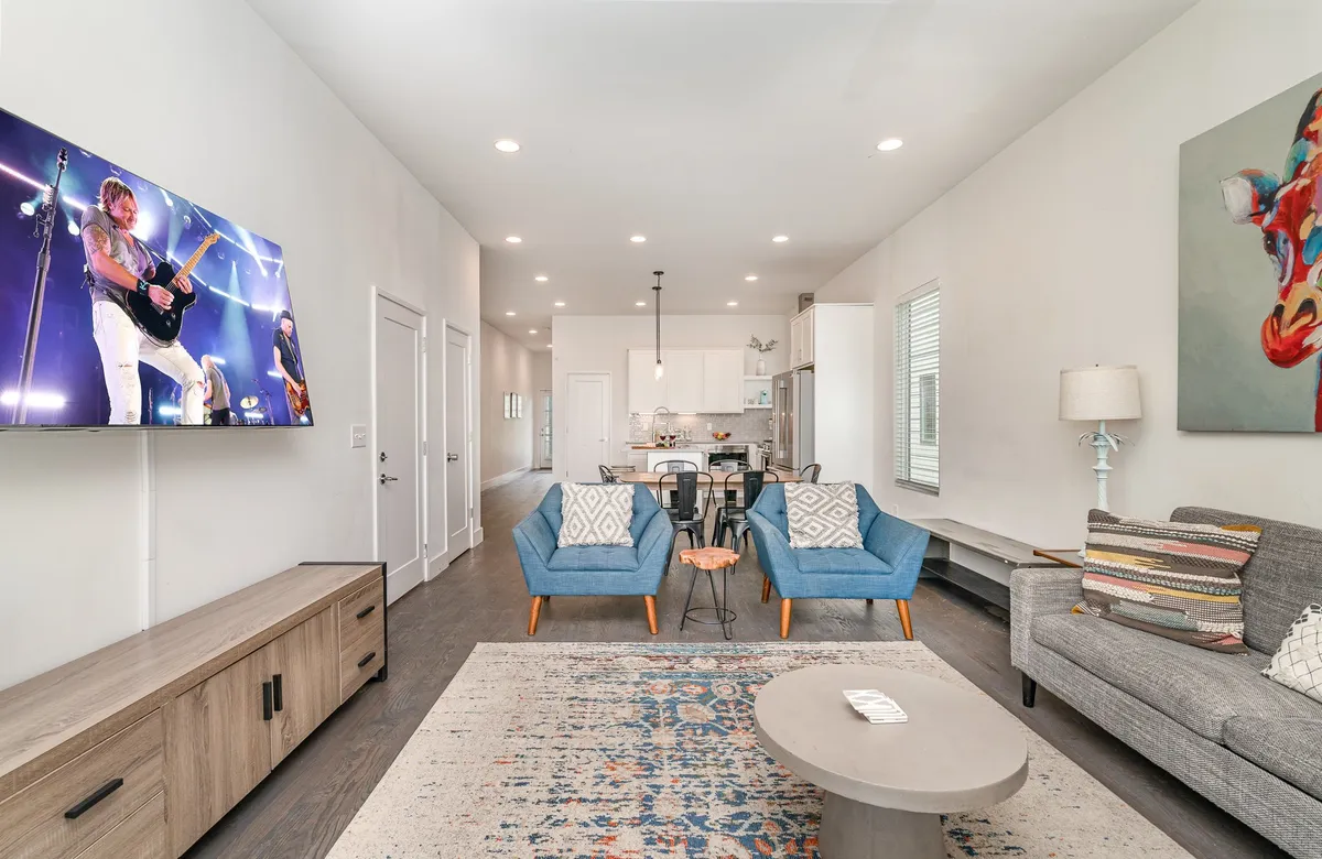 Contemporary living space with blue armchairs facing a large television displaying a vibrant live concert, complemented by wall art and an inviting atmosphere. The setting is perfect for socializing, relaxing, or catching a show together.